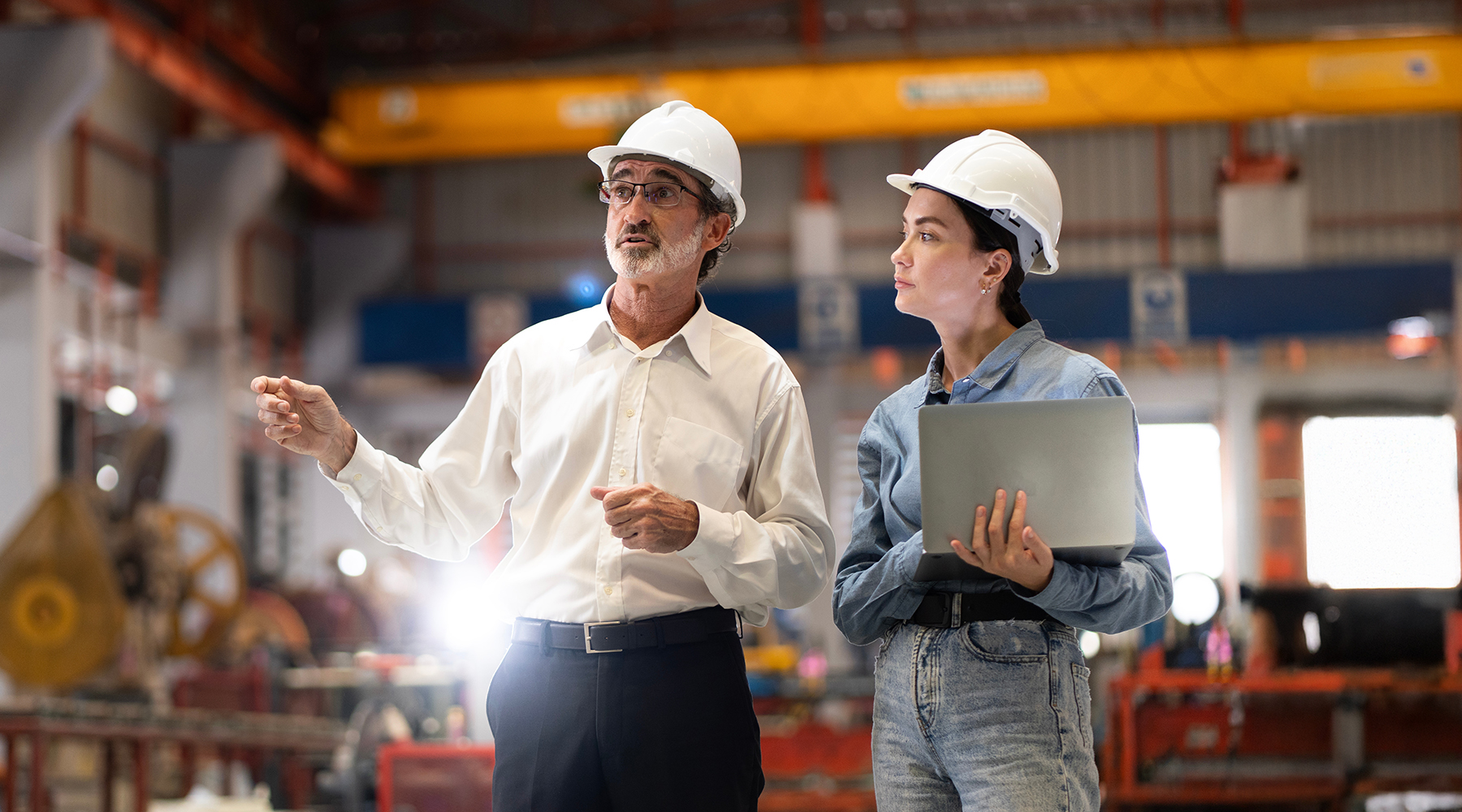 two professional engineers wearing hard hats discussing notes on site